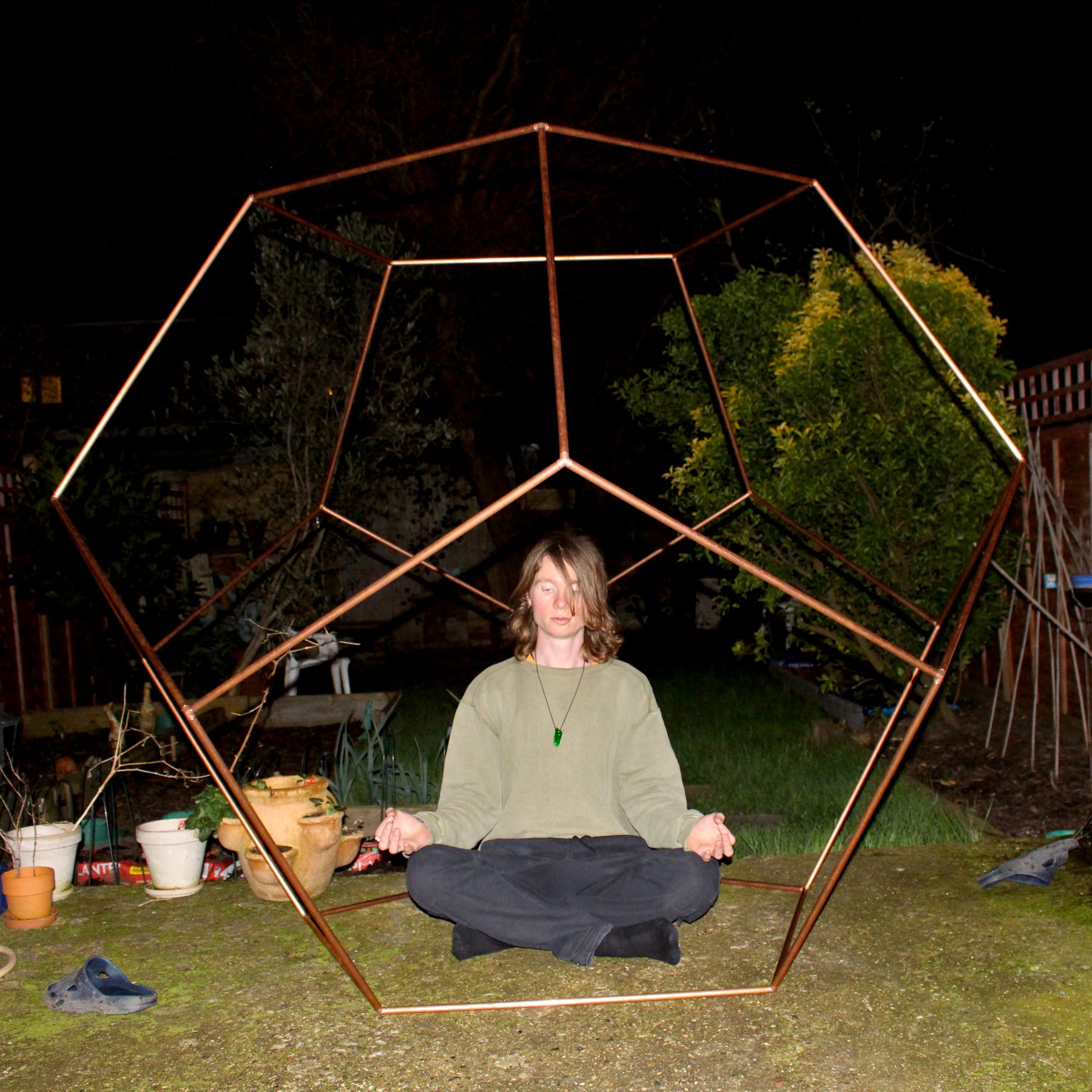 Person meditating inside a geometric metal structure at night.