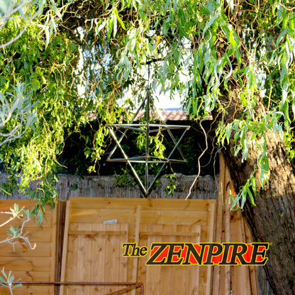A copper hanging merkaba ornament suspended outdoors beneath weeping willow branches in front of a wooden fence and tree trunk