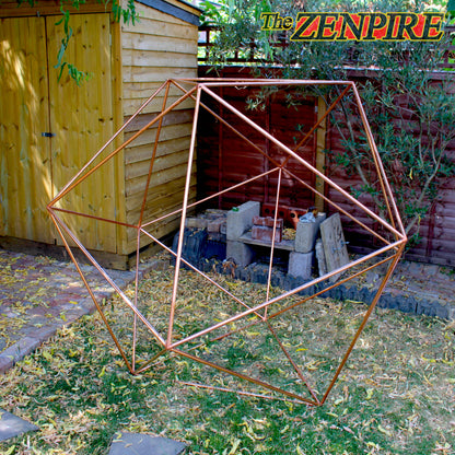 A geometric icosahedron wireframe structure made of copper pipe, displayed outdoors in a backyard garden setting.