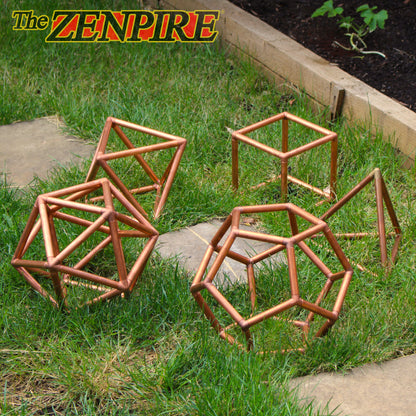 an array of large copper platonic solids featuring dodecahedron, icosahedron,. octahedron, cube and tetrahedron laid out on the grass