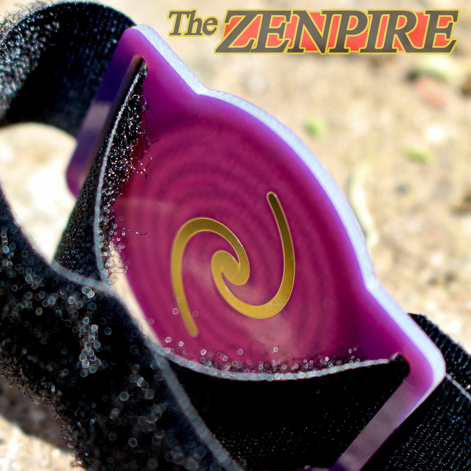 A close-up of a black wristband with a translucent purple and magenta visor featuring a gold krystal spiral