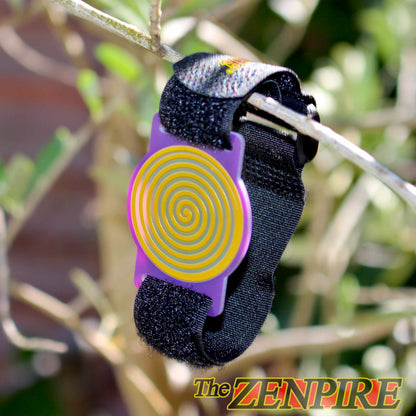 A black wristband with a purple and gold healing spiral, shown hanging from a tree branch outdoors