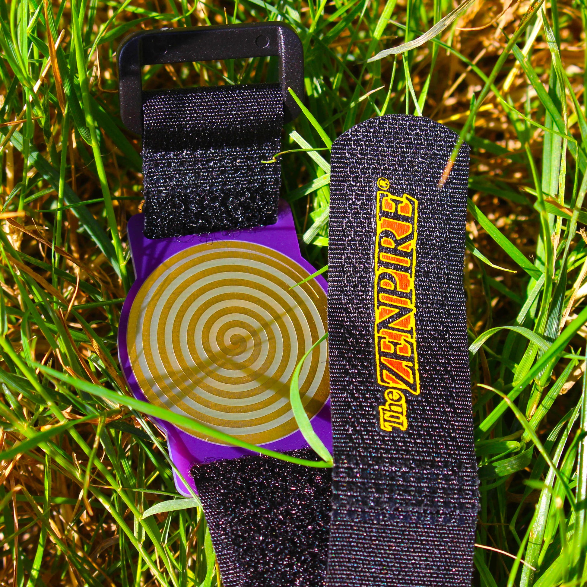 A wristband with a purple case and a gold healing spiral, attached to a black fabric strap.