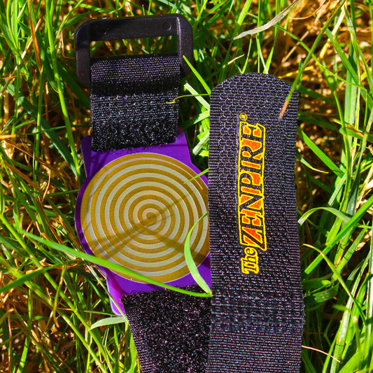 A wristband with a purple case and a gold healing spiral, attached to a black fabric strap.