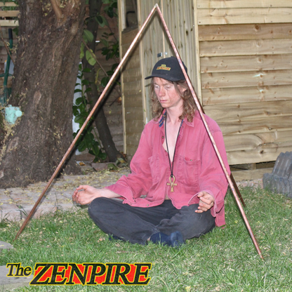 Person meditating outdoors with a copper pyramid kit structure and tree in the background, By The Zenpire