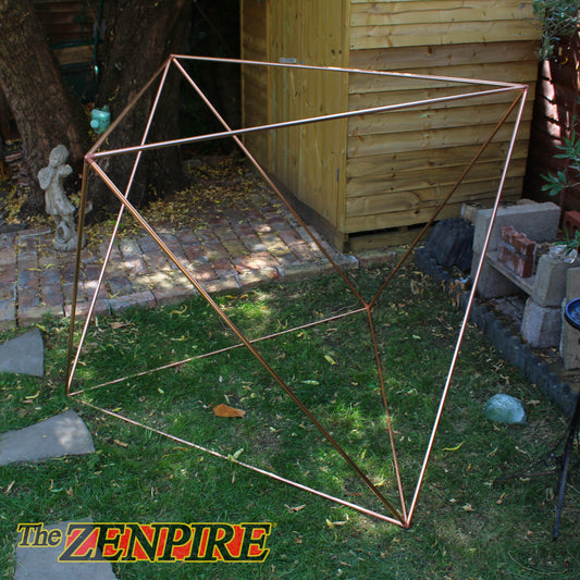 A geometric octahedron wireframe structure made of copper pipes, set outdoors on a grassy lawn, used for meditation.