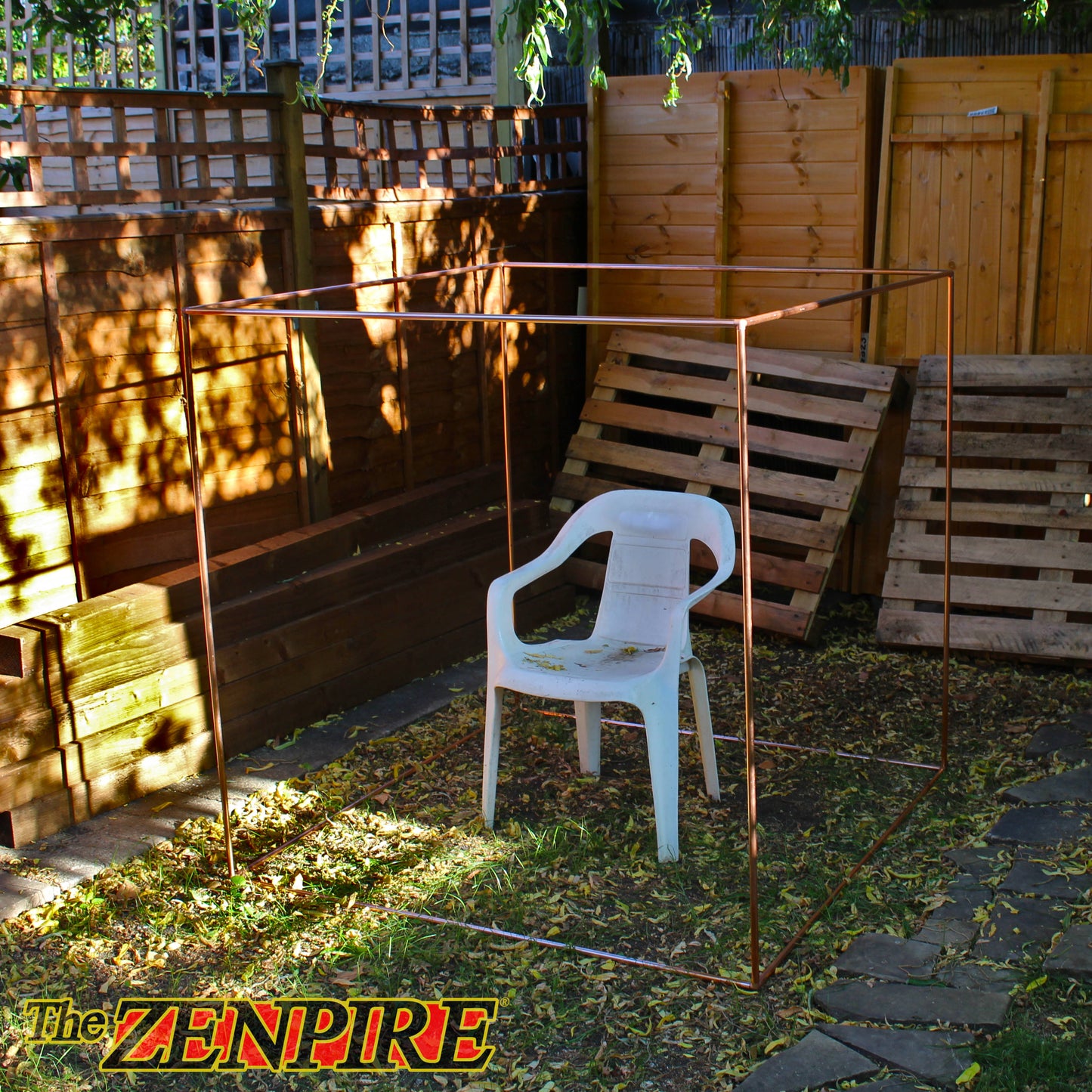 A copper metal cube frame for meditation set up in an outdoor backyard with a white plastic chair placed in the center.