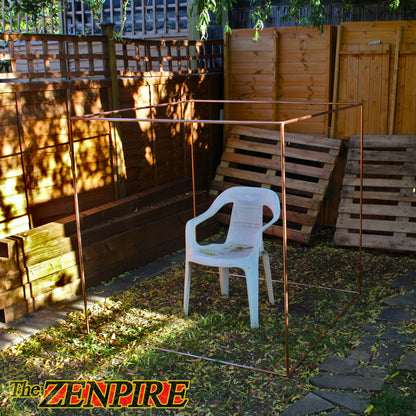 A copper metal cube frame for meditation set up in an outdoor backyard with a white plastic chair placed in the center.