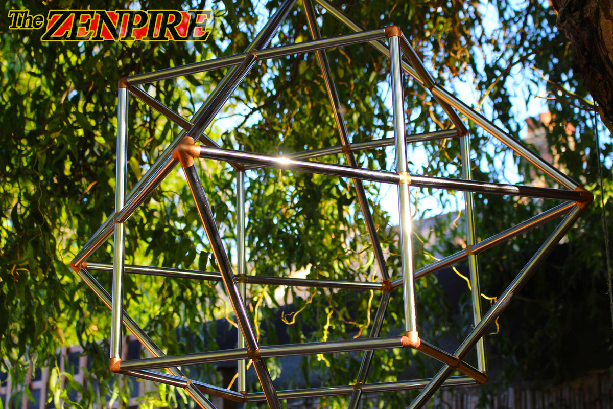 a sacred geometry cube octahedron made from chrome copper pipes and connectors hanging beautifully with a tree background